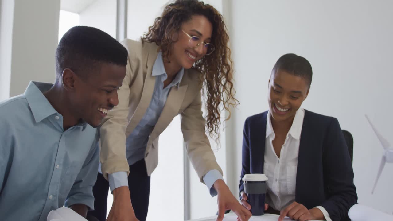 Biracial smiling female and male architects talking and checking architects plans in modern office