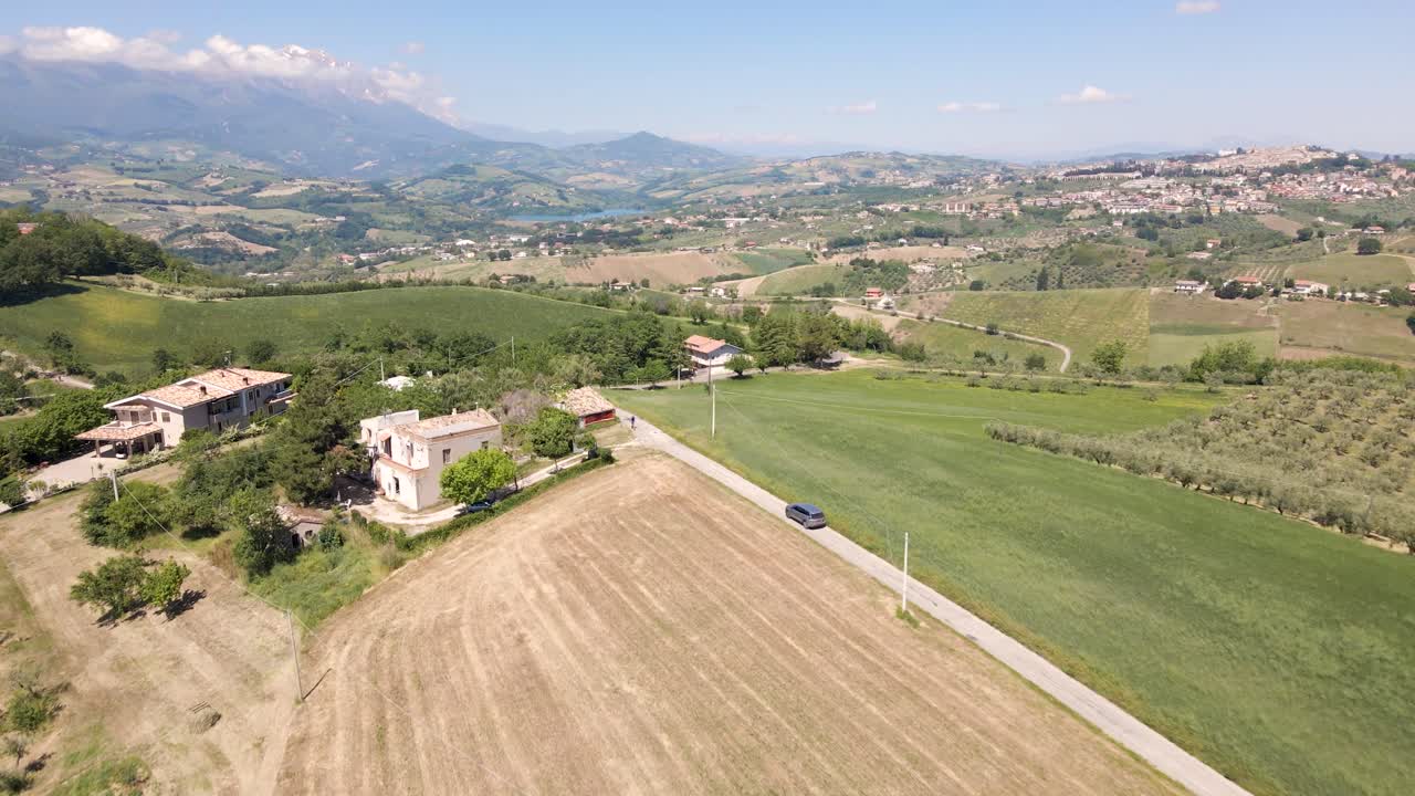 disparo de dron de gran angular rastreando un vehículo conduciendo en el campo remoto de italia rodeado por una hermosa vista de viñedos, olivos y una cadena montañosa ubicada en abruzzo, italia