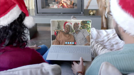 Happy-diverse-couple-and-senior-parents-having-christmas-laptop-video-call,-slow-motion