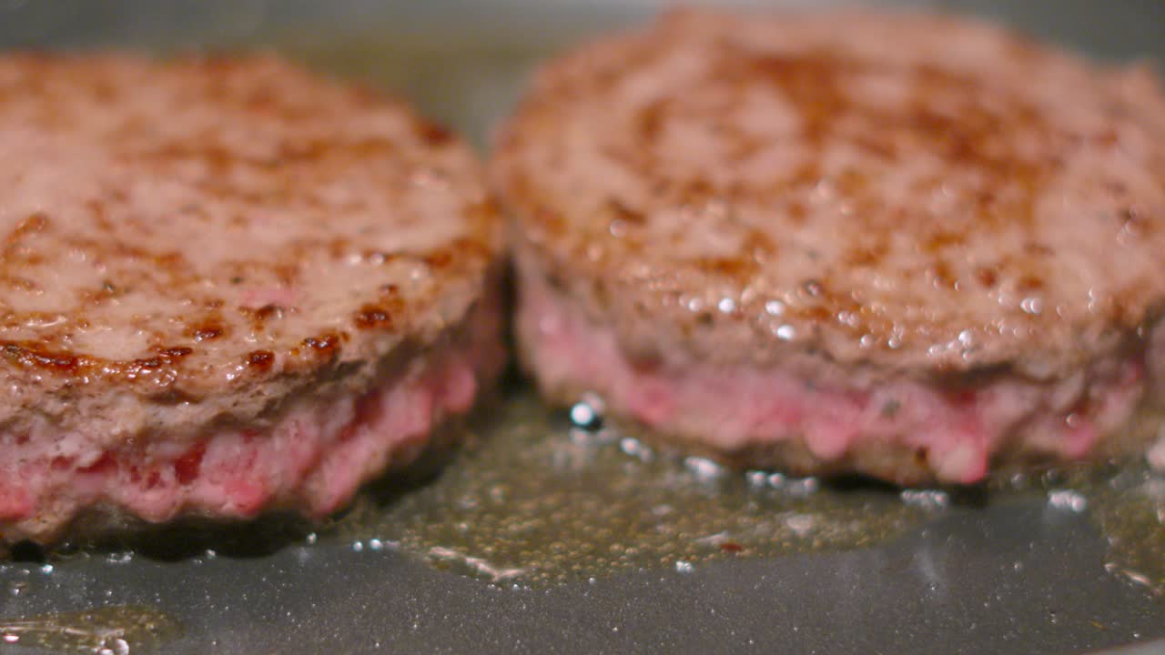 Delicious Beef Burgers Cooking with Fat Oozing Out as Meat Cooks in Bubbling Hot Oil. Slow Motion Close Up Food Clip