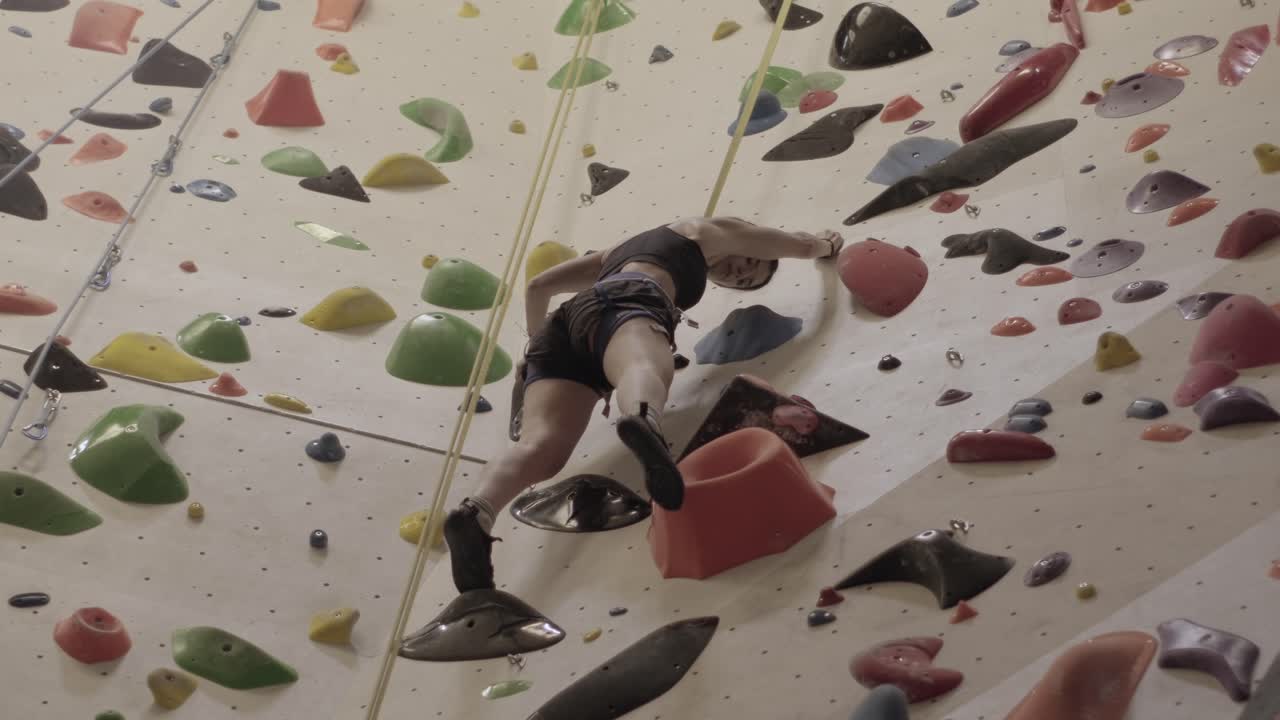 mujer abordando una pared de escalada interior desafiante, agarres vibrantes