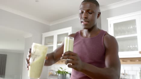 happy african american man drinking healthy smoothie in kitchen at home, slow motion