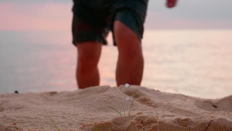 asian young guy walking towards camera with focused beach sand at sunset time