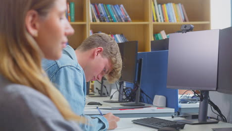 male university or college student working at computer in library being helped by tutor