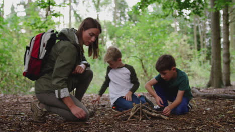 Teamleiterin-Mit-Jungen-Im-Outdoor-Aktivitätslager,-Das-Gemeinsam-Feuer-Im-Wald-Aufbaut