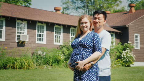 young multi-ethnic couple - asian man and pregnant caucasian woman are standing in front of their ne