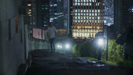 european man male caucasian white model going up in the night with lights in the city town on the top of the hill and steps with long hair