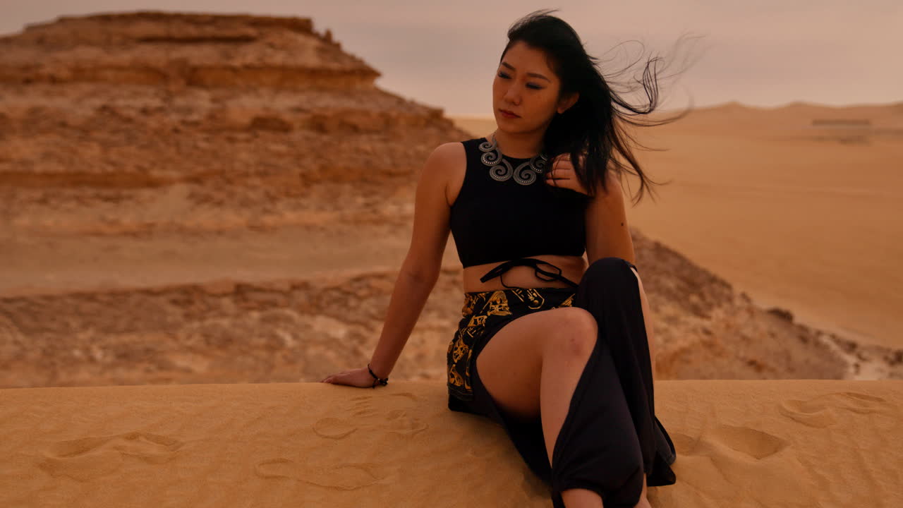 mujer sentada en una duna de arena en el desierto y posando en trajes tradicionales