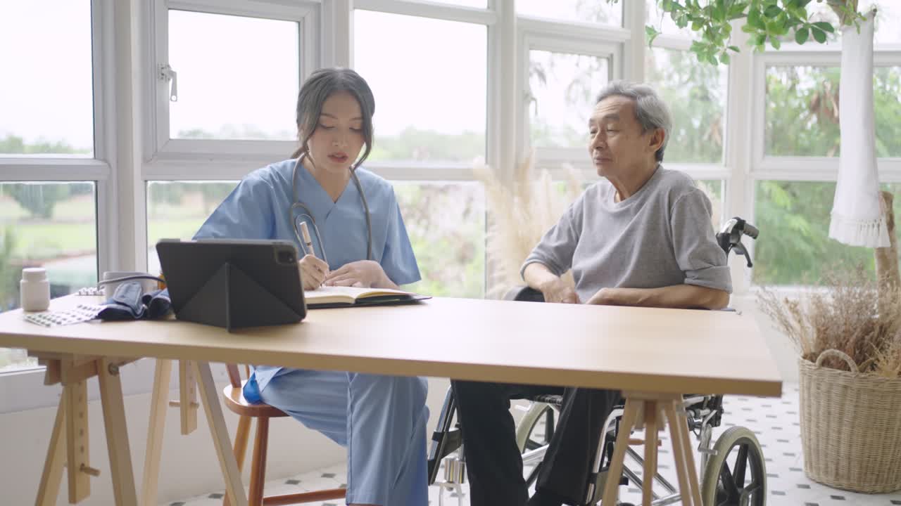 車椅子に乗った高齢の男性患者と話しながら病気を診断する若いアジア人看護師