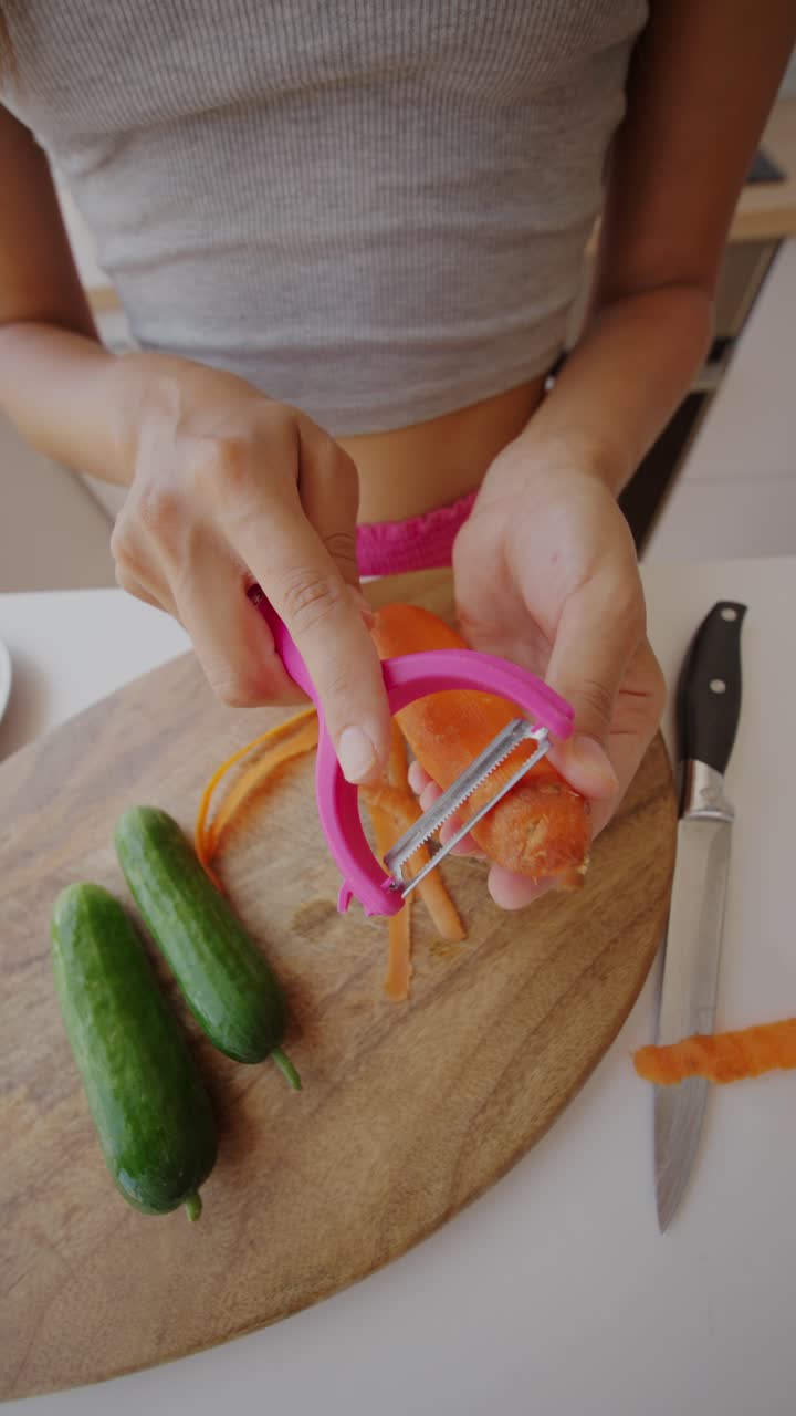 Person peeling a carrot on a wooden cutting board with cucumbers