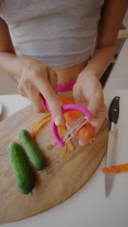 person peeling a carrot on a wooden cutting board with cucumbers
