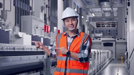 asian male engineer with safety helmet smiling and pointing to side while standing at pharmaceutical factory, vaccine production facility
