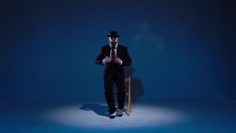 a man in a suit and hat smoking in a spotlighted studio
