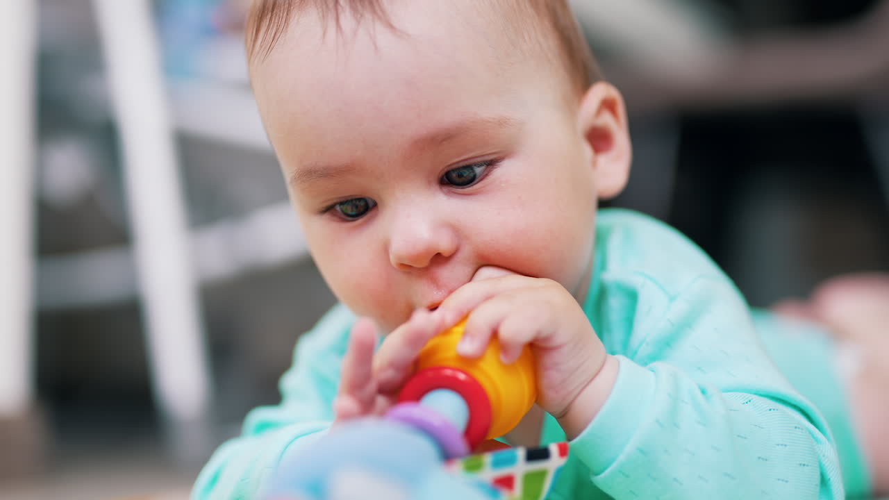 Darling little boy is busy playing with his toy. Child lies on belly waving with a toy. Close up. Blurred backdrop.