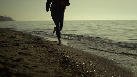 unknown girl jogging sandy beach. slim woman legs running at sunset outside.