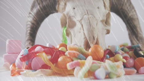 light trails over halloween candies and goat horns and skull against white background