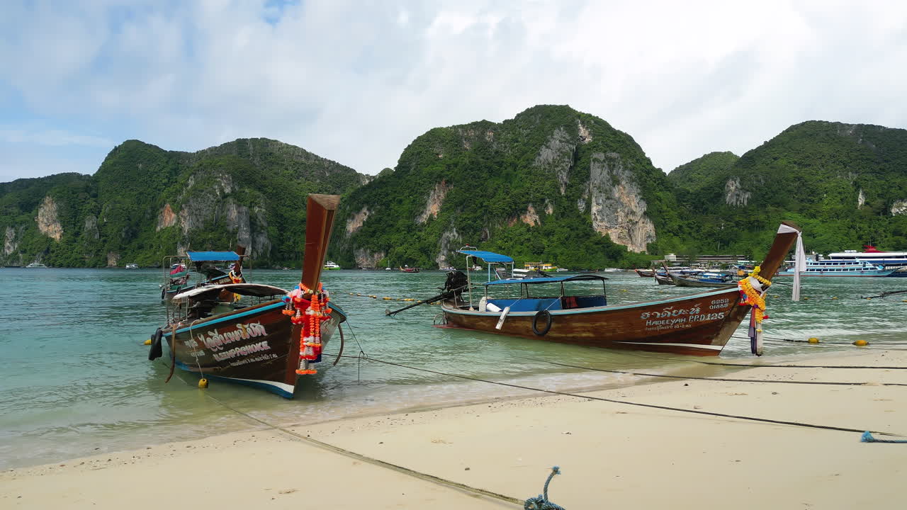 Tradizionali barche longtail sulla costa del Mare delle Andamane all'isola di Phi Phi, Thailandia, ripresa in allontanamento.