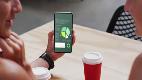 hombre y mujer caucásicos sentados a la mesa, usando un teléfono inteligente con estadísticas en la pantalla