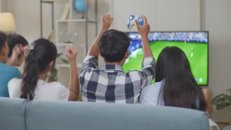 asian teenagers playing soccer video games and celebrating victory at home