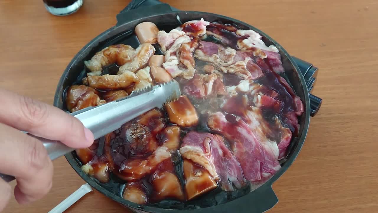 맛있는 일본식 고기 요리, 굽고, 지글지글 끓고, 부엌에서 데리야키 소스를 곁들인 내부 검은 팬에 튀기고, 은색 집게를 들고 백인 손가락으로 회전하고, 오버헤드 정적인