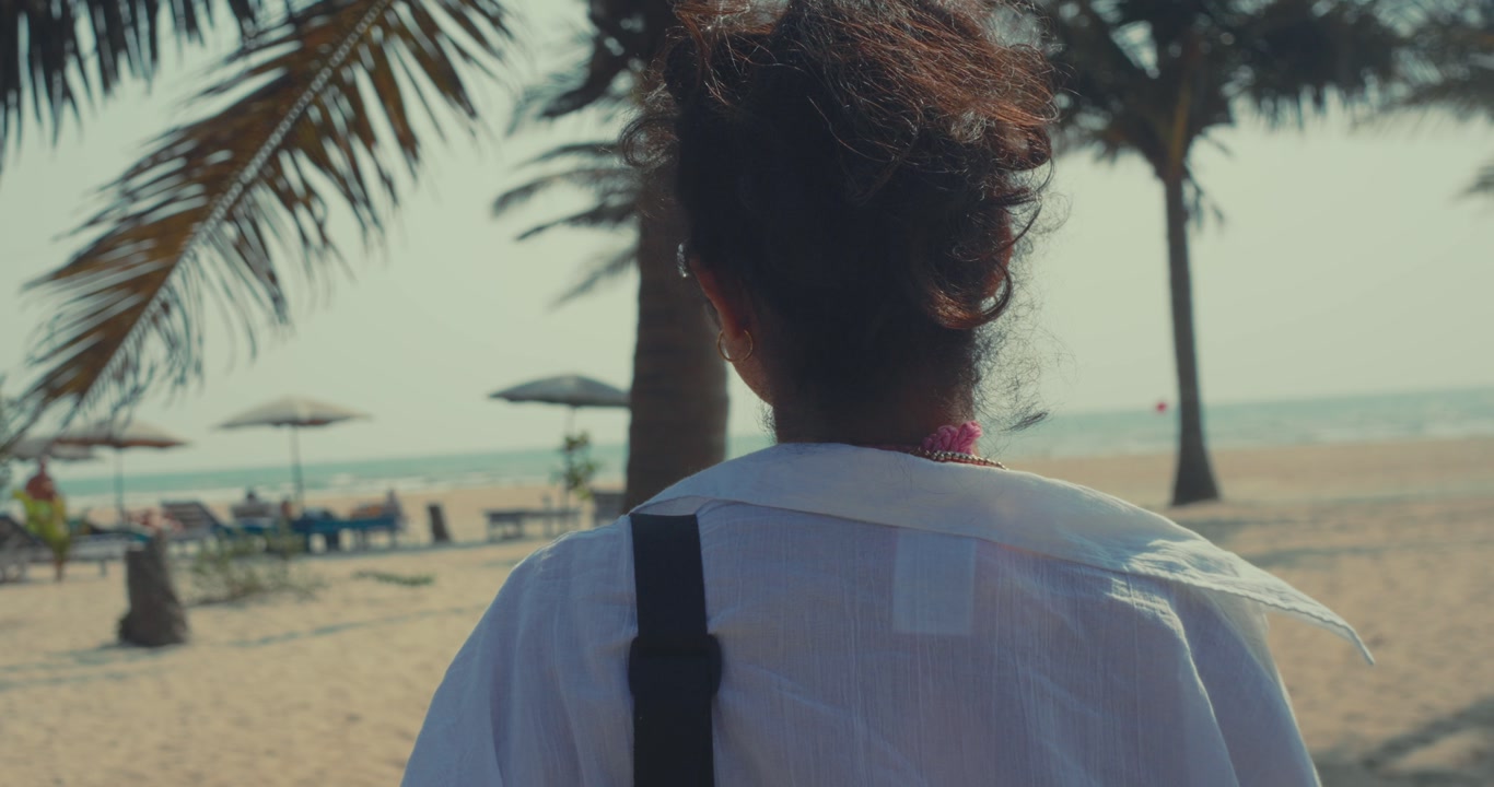 Back view of woman walking on sandy beach with palm trees and ocean calm travel lifestyle scene