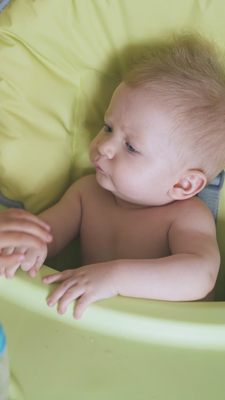 careful little girl in white t-shirt calms by stroking cute baby sitting in green soft highchair in light room