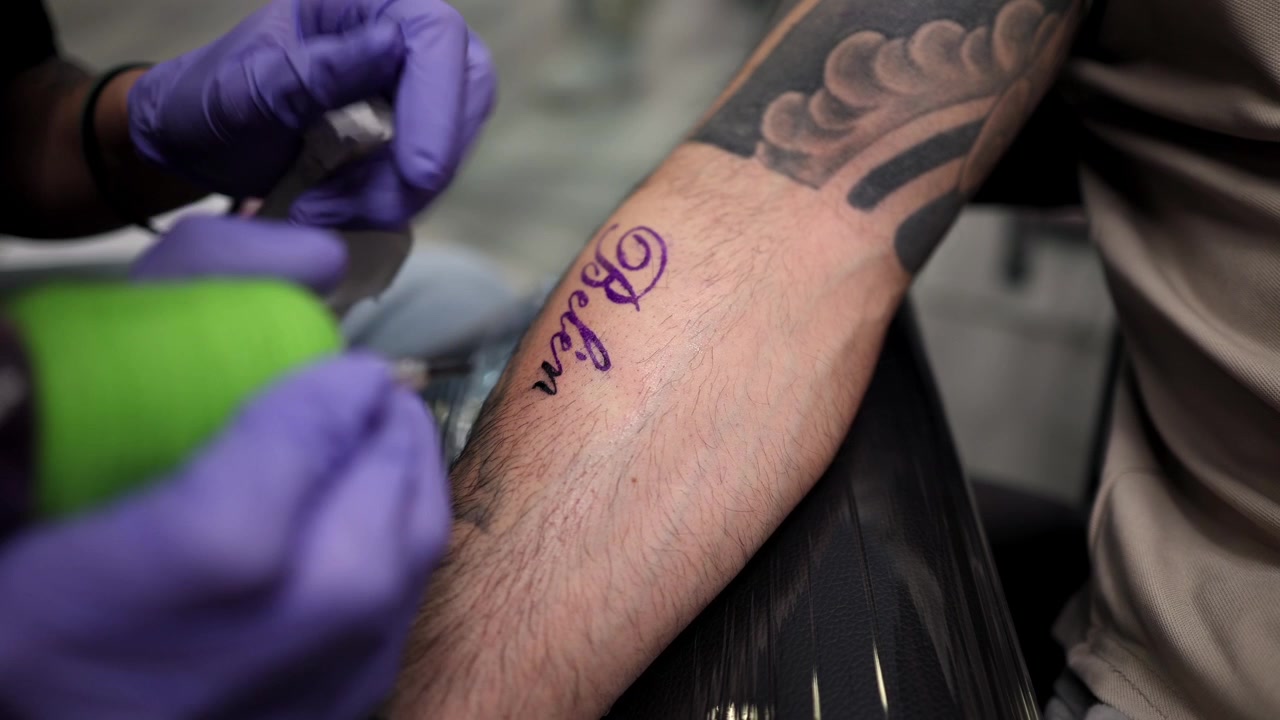 Tatuatore che lavora a un tatuaggio con scritta sul braccio di un cliente