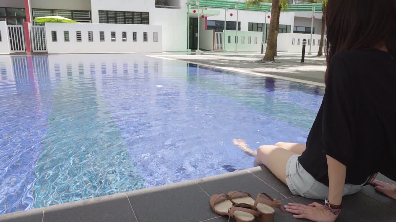 girl sitting down while splashing her legs in swimming pool
