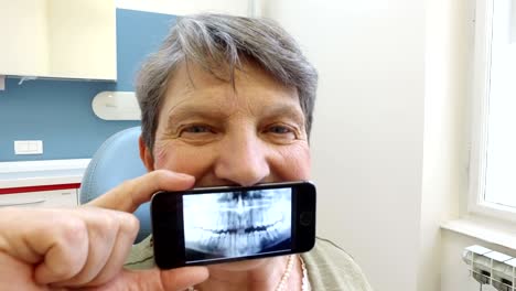 elderly woman holding smartphone with photo of dental x- ray