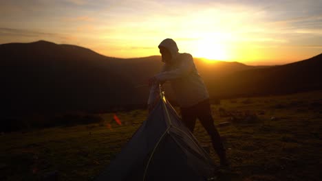 backpacking man preparing pitching camping tent in sunset wilderness