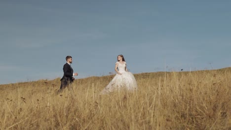 Newlyweds.-Caucasian-groom-with-bride-running-on-mountain-slope.-Wedding-couple