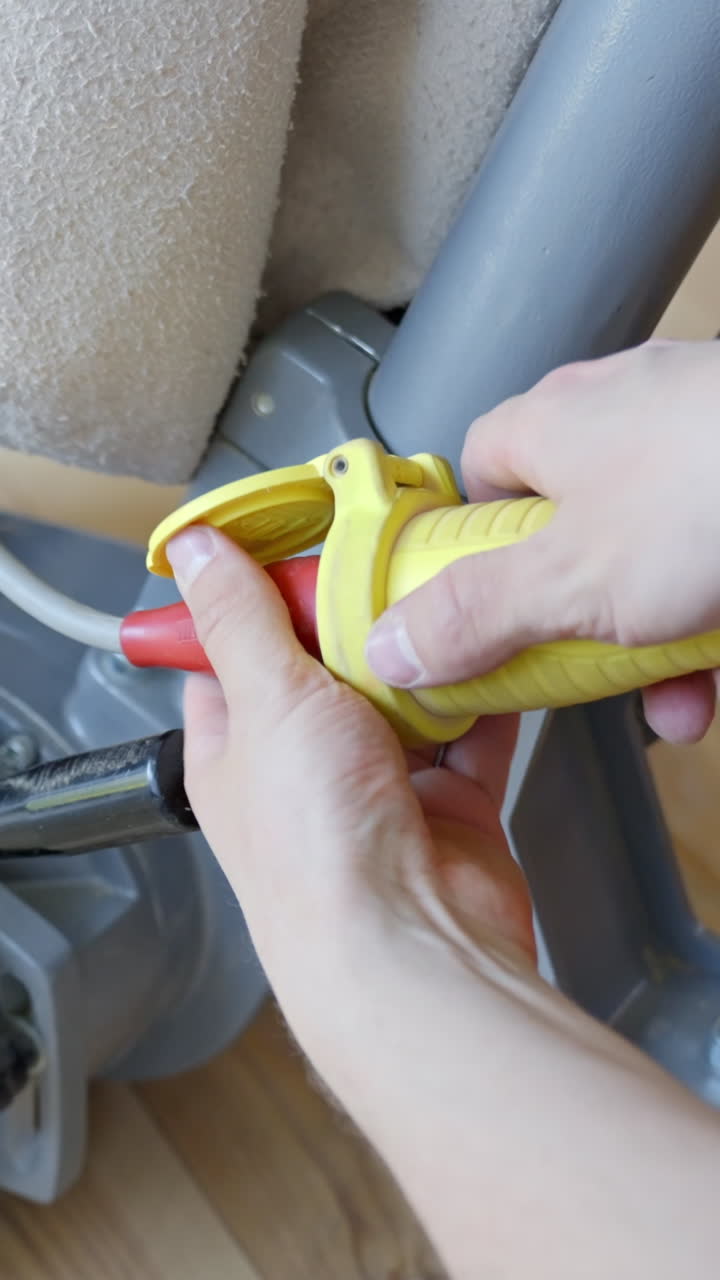 Unrecognizable person hands unplug a yellow power cord from a floor sanding machine after use, showing technical grip and safety gesture in a close-up vertical frame, static camera, real time