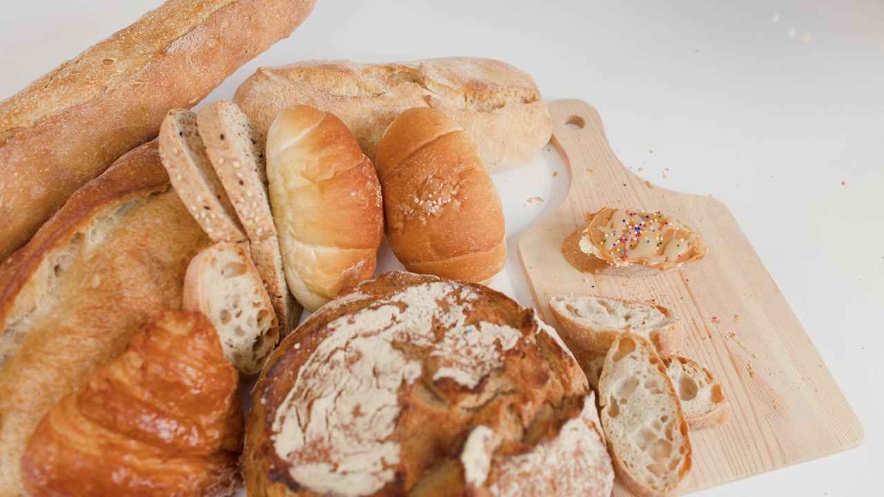 Overhead view of sourdough, baguettes, and croissants with colorful sprinkles falling on wooden board.