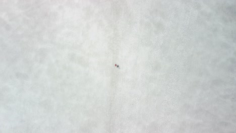 top down aerial view of two hikers walking on white snow and ice covered landscapes in iceland during a clludy day. people are walking forward and drone moves with them with smooth motion.