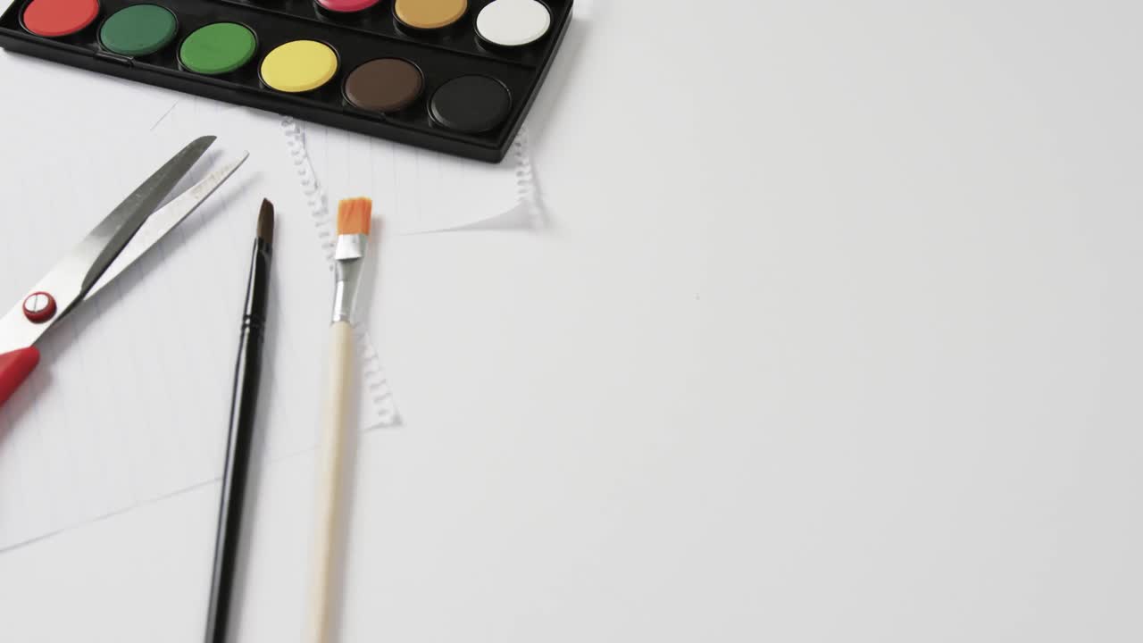 Close up of paints, brushes and scissors on white background with copy space, in slow motion