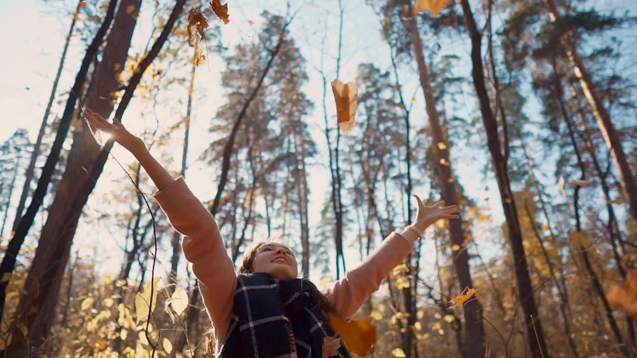 mujer arrojando hojas en un bosque de otoño