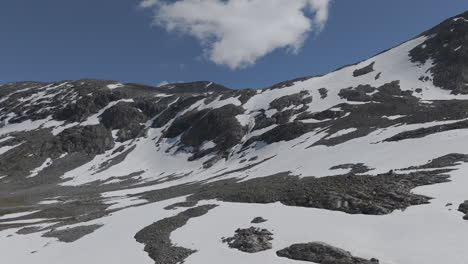 un avión no tripulado en cámara lenta volando hacia una poderosa cascada cerca del lago langvatnet en noruega cerca de strynefjellsveg rompiendo a través del hielo y la nieve en un día soleado rodeado de rocas brillantes