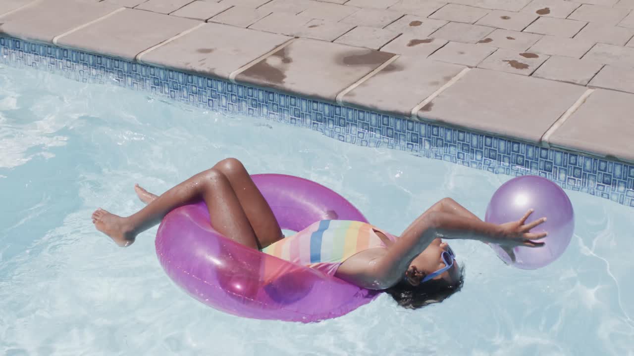 Happy african american girl sitting in swim ring in swimming pool, slow motion