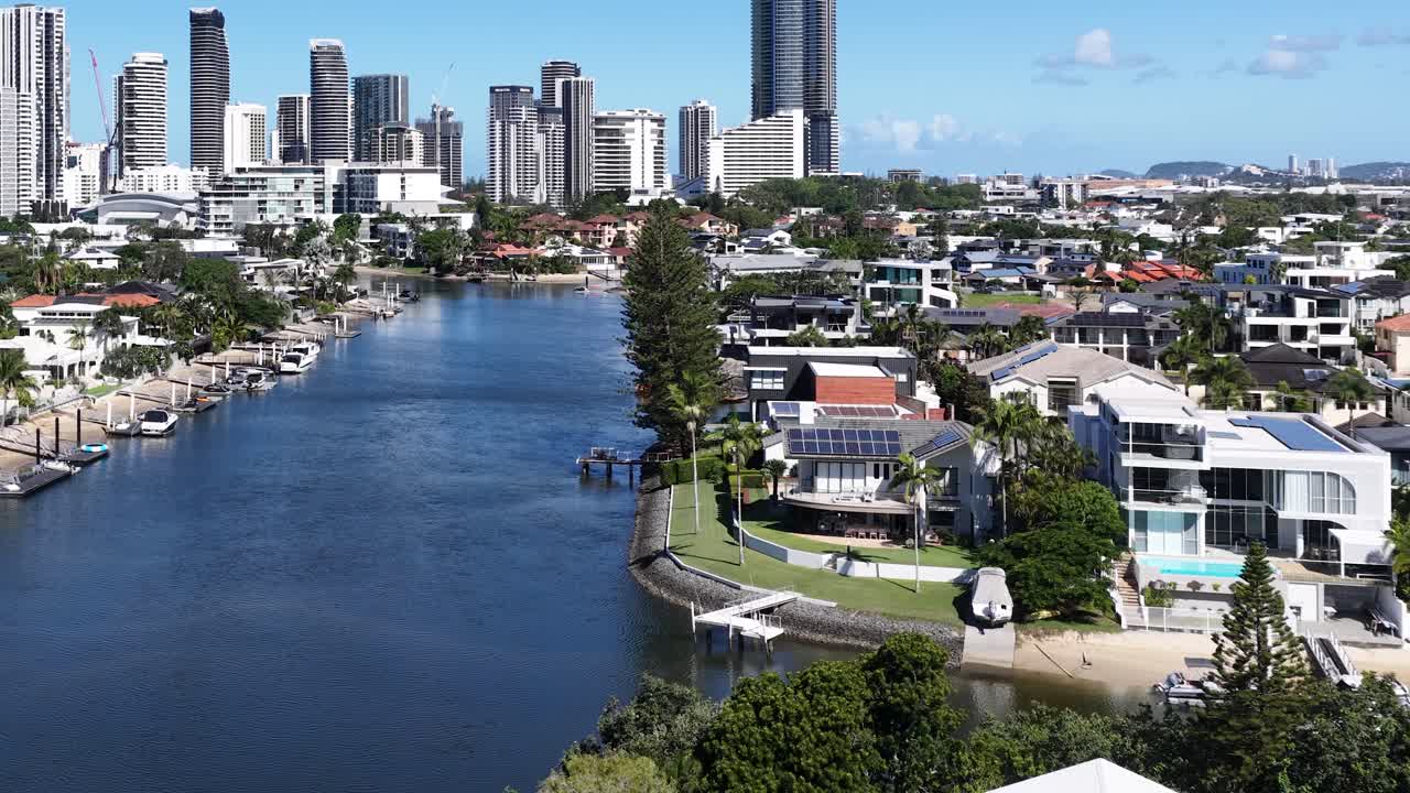 Voo de drone sobre um canal azul em direção a mansões de luxo e o horizonte distante da cidade.