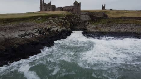 tracking shot of dunstanburgh castle - fast hover over water before ascending above the castle