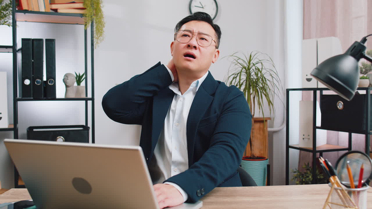 Tired asian businessman suffers from spine neck muscle hard pain at office workplace overworking