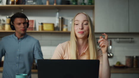 Woman-consulting-online-video-call-on-kitchen-while-guy-dancing-on-backdrop.