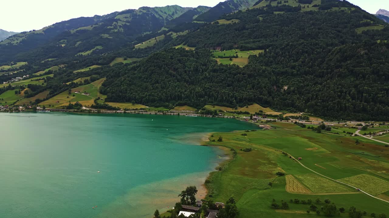 vista panorámica de una aldea frente al lago, campo verde exuberante, lago prístino, rodeado de grandes montañas cubiertas de árboles
