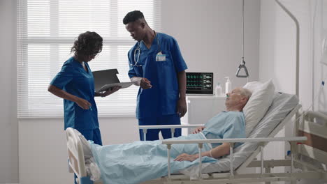 two african american doctors a man and a woman examine and talk to an elderly patient lying on a bed in a hospital