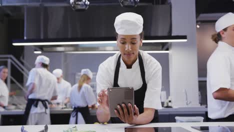 chef afroamericana vestida con ropa blanca en una cocina de un restaurante, usando una tableta