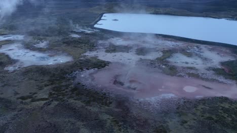 toma aérea inclinada hacia abajo del paisaje geotérmico volcánico con ollas de barro de cráter hirviendo durante el día nublado en islandia, europa