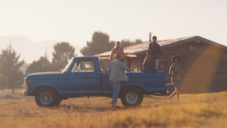 Gruppe-Von-Freunden-Entlädt-Rucksäcke-Vom-Pick-up-Truck-Auf-Dem-Roadtrip-Zu-Einer-Hütte-Auf-Dem-Land