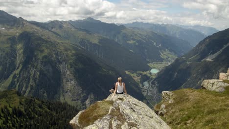 young woman sitting on a cliff on top of a mountain and enjoying the amazing mountain view in the tirolean alps