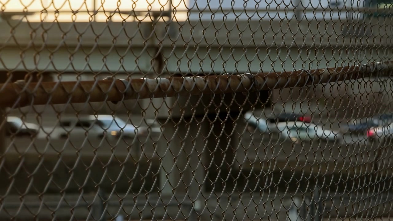 Coches circulando por un puente en un entorno industrial, con estructuras y vallas metálicas, textura de hormigón, desde una perspectiva lateral del puente.