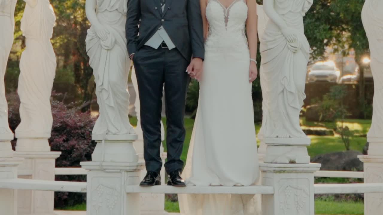 la novia y el novio se mantienen de mano en una plataforma de mármol en un jardín